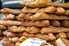 Stacks of freshly baked rye and wheat loaves in an artisan bakery with a handwritten sign.
