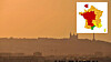 Hazy orange sunset over a silhouetted city skyline with a church tower and communications mast.
