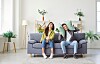 Young couple on a sofa covering their ears in a bright living room.