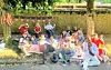 Group of people sitting on blankets and chairs at an outdoor picnic under trees with bunting overhead.