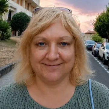 Woman standing on a street with parked cars and buildings at sunset.
