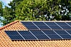 Solar panels mounted on a terracotta-tiled roof with trees in the background.