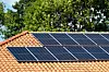 Solar panels mounted on a terracotta-tiled roof with trees in the background.