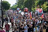 Large crowd marching along a tree-lined avenue in Paris during a public protest, with flags and banners visible.