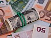 A tied stack of US $100 bills resting on euro banknotes.