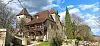 Historic stone house with red roofs, timber balconies and stone walls beneath a blue sky.