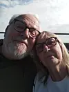 Ken Jones and wife taking a close selfie outdoors with a bright sky behind them.