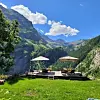 Outdoor terrace with sun umbrellas and seating overlooking a green mountain valley.