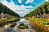 River running through Bar-le-Duc town centre with trees, grass and buildings on both banks.