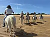 Riders on horses cross a sandy plain beneath a clear blue sky.