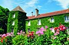 Ivy-covered stone house behind a colourful flower garden under a blue sky.