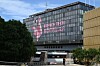 Glass-fronted building in Montpellier with a large pink TECH sign and trees in the foreground.