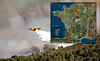 A firefighting aircraft drops water on a smoky wildfire over a forested hillside near the coast.