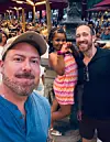 Three people pose for a selfie at a busy outdoor dining venue.