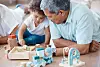 Little girl playing with wooden toys beside an older man at a table