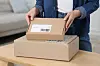 Woman opening a cardboard parcel on a wooden table at home.