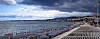 Pebble beach and seafront promenade along Nice, France, beneath a cloudy sky