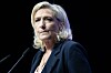Marine Le Pen speaks at a podium against a dark background in Châlons-en-Champagne, France.