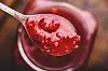 Spoonful of raspberry jam held above an open glass jar