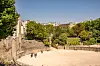 Aerial view of a tree-lined stone courtyard with visitors and Paris rooftops beyond