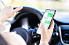 Driver holds a smartphone over a steering wheel inside a car.