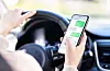 Driver holds a smartphone over a steering wheel inside a car.