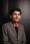 Man in a grey suit and red bow tie posed against a dark studio backdrop