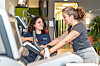 Fitness instructor assists a woman using exercise equipment in a gym.