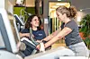 Fitness instructor assists a woman using exercise equipment in a gym.