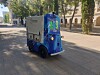 Blue autonomous cleaning vehicle on a tree-lined urban plaza