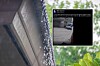 Rainwater cascades from a house roof beside blurred green foliage.