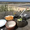 Pot of mussels, chips and bowls of food on a seaside table overlooking a beach