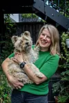 Smiling woman holding a small shaggy dog in a leafy garden