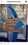 Blue inflatable figure holding a handwritten protest placard outside a shuttered shop