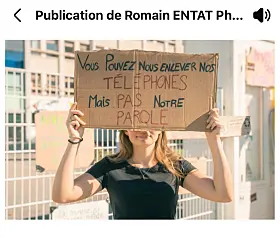 Masked demonstrator holding a handwritten French protest sign outside a building
