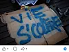Torn cardboard with large blue spray-painted lettering on a dark wooden surface