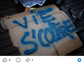 Torn cardboard with large blue spray-painted lettering on a dark wooden surface