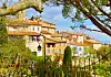 Terracotta-roofed buildings and gardens in Mougins, France, framed by trees and a wrought-iron fence.