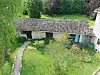 Weathered stone outbuilding with a tiled roof beside a garden path and flowering plants
