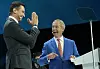 Nigel Farage and Jordan Bardella gesture on stage beside a lectern at a Reform UK conference.