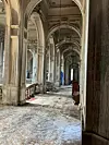 Ornate stone colonnade with arches, columns and patterned flooring leading to a distant doorway