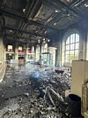 Debris fills a damaged historic interior beneath ornate ceilings and tall arched windows.
