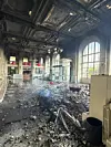 Debris fills a damaged historic interior beneath ornate ceilings and tall arched windows.