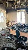 Damaged room with rubble, overturned chairs, broken desks and an exposed ceiling