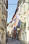 Narrow old street with stone buildings, coloured shutters and overhead wires in Cuers, southern France