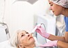 Dermatologist uses a radiofrequency device on an older woman’s face in a clinic.