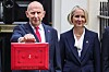 Two politicians pose outside a building, one holding a bright red parliamentary dispatch box.